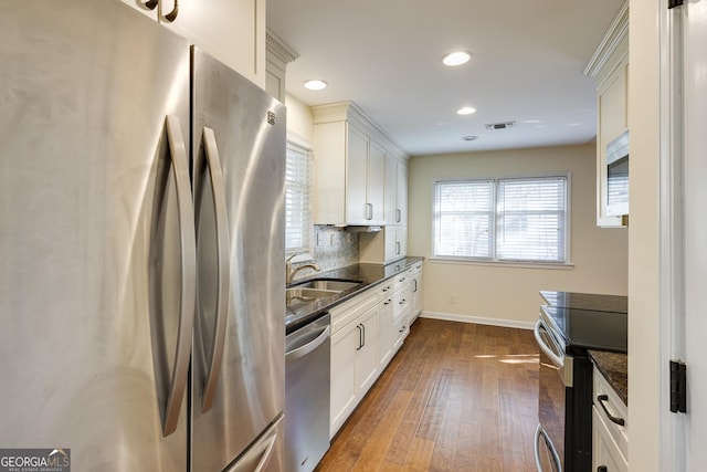 kitchen with white cabinets, dark wood-style flooring, a sink, stainless steel appliances, and baseboards