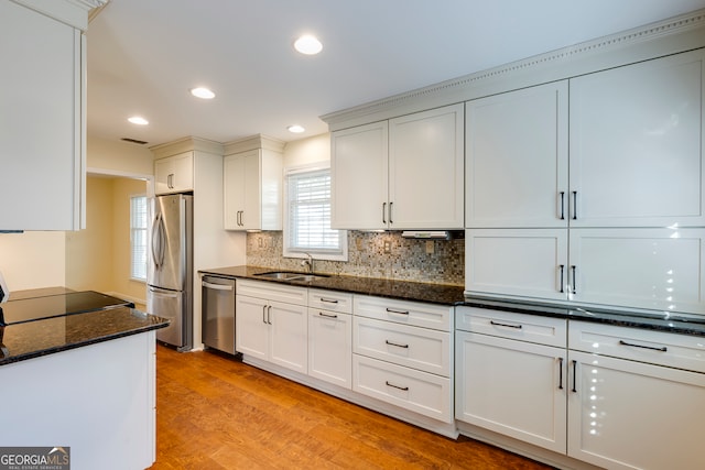 kitchen featuring white cabinetry, sink, dark stone countertops, appliances with stainless steel finishes, and light wood-type flooring