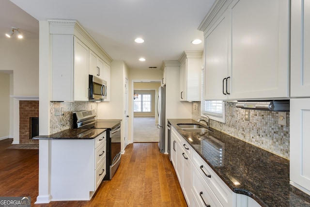 kitchen with wood finished floors, a sink, baseboards, dark stone countertops, and stainless steel appliances