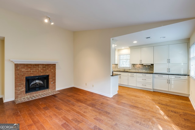 kitchen featuring backsplash, a brick fireplace, sink, light hardwood / wood-style floors, and white cabinetry