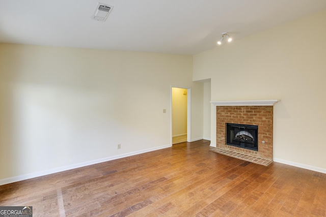unfurnished living room featuring visible vents, baseboards, a brick fireplace, and wood finished floors
