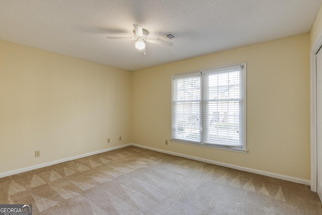 empty room with a textured ceiling, ceiling fan, light colored carpet, and baseboards