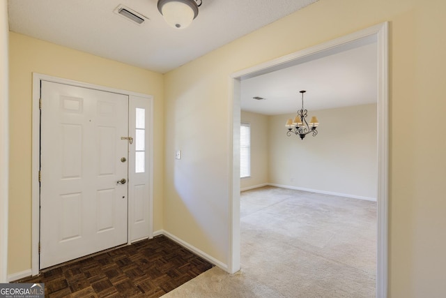 entryway featuring baseboards, visible vents, dark colored carpet, and a notable chandelier