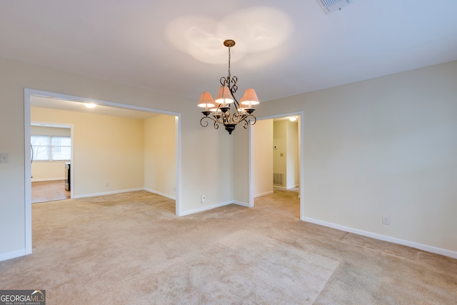 spare room featuring light carpet and a chandelier