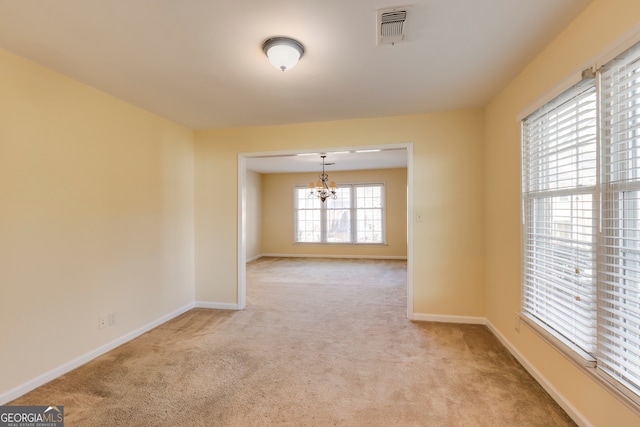 spare room featuring light carpet and a chandelier