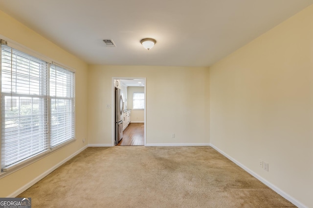 unfurnished room featuring baseboards, light carpet, and visible vents