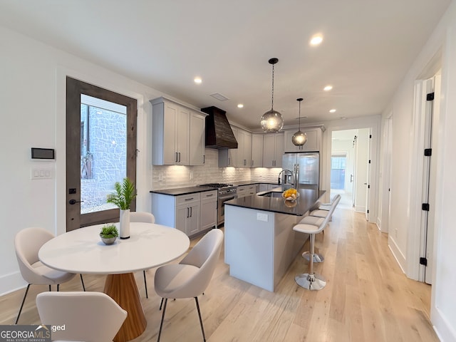 kitchen featuring light wood-style flooring, a sink, custom range hood, appliances with stainless steel finishes, and dark countertops