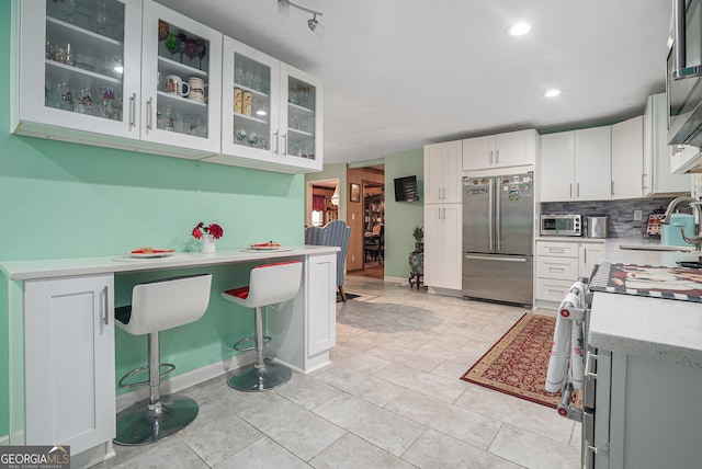 kitchen with sink, decorative backsplash, a breakfast bar, white cabinets, and appliances with stainless steel finishes