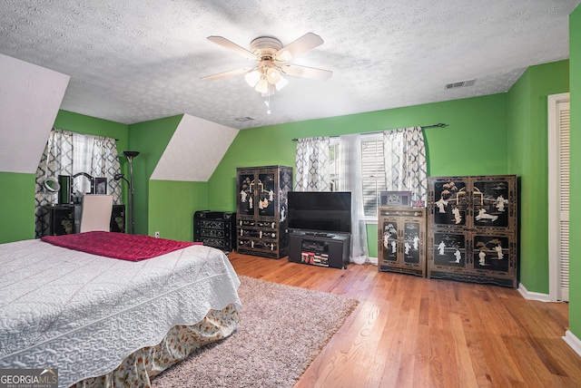 bedroom with hardwood / wood-style floors, ceiling fan, a textured ceiling, and vaulted ceiling