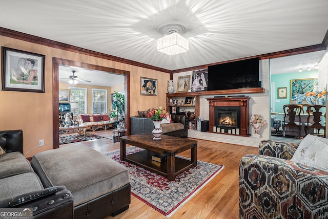 living room featuring a fireplace, crown molding, hardwood / wood-style floors, and ceiling fan with notable chandelier