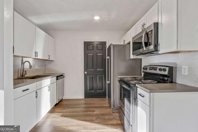 kitchen with backsplash, sink, light hardwood / wood-style flooring, appliances with stainless steel finishes, and white cabinetry