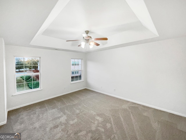 unfurnished room with a raised ceiling, ceiling fan, and carpet