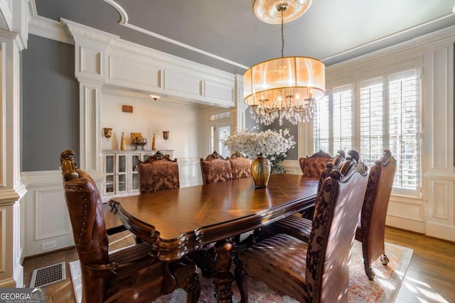 dining space featuring a notable chandelier, light wood-type flooring, ornamental molding, and ornate columns