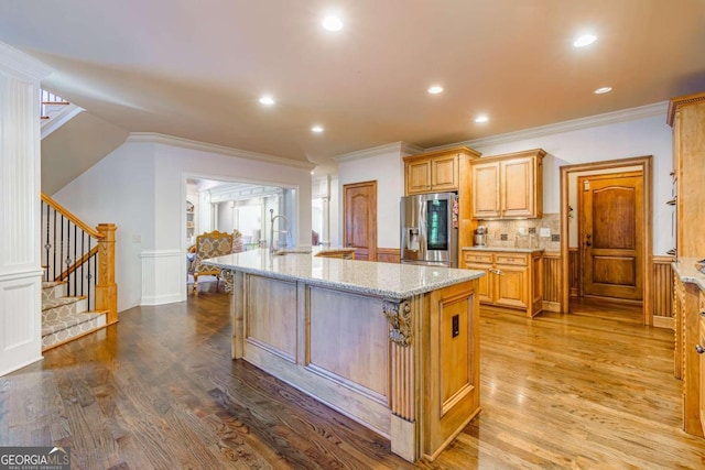 kitchen with a center island with sink, light hardwood / wood-style floors, light stone countertops, and stainless steel refrigerator with ice dispenser