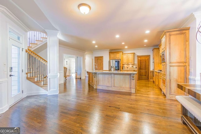 kitchen featuring stainless steel refrigerator with ice dispenser, ornate columns, ornamental molding, a kitchen island with sink, and light hardwood / wood-style floors