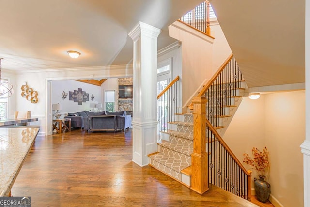 stairs featuring hardwood / wood-style floors, a stone fireplace, ornamental molding, and ornate columns