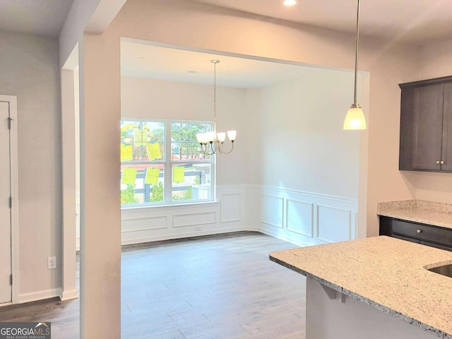 kitchen with light stone countertops, dark brown cabinets, decorative light fixtures, a notable chandelier, and dark hardwood / wood-style floors