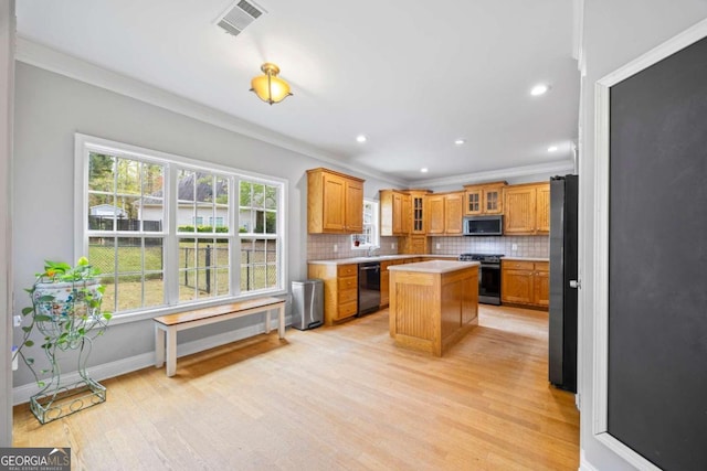 kitchen with tasteful backsplash, ornamental molding, black appliances, light hardwood / wood-style flooring, and a center island