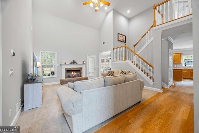 living room with ceiling fan, a fireplace, high vaulted ceiling, and light hardwood / wood-style flooring