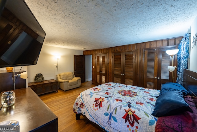 bedroom featuring a textured ceiling, wooden walls, and light hardwood / wood-style flooring