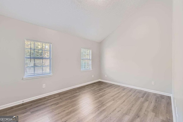 spare room with hardwood / wood-style floors, lofted ceiling, a textured ceiling, and a wealth of natural light