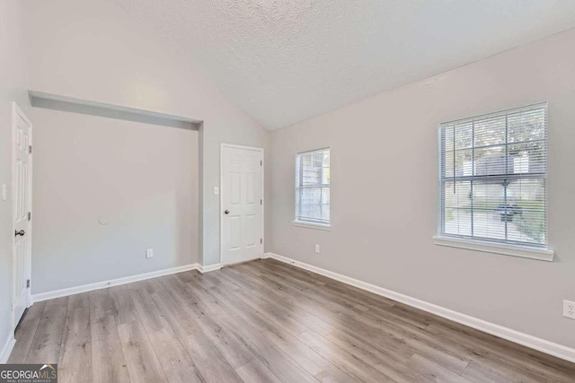 unfurnished bedroom with a textured ceiling, light hardwood / wood-style flooring, and lofted ceiling