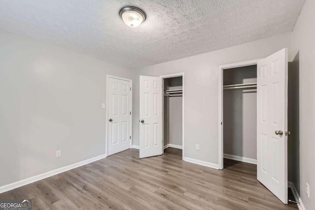 unfurnished bedroom featuring wood-type flooring, a textured ceiling, and two closets