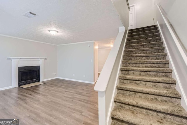 stairs with a textured ceiling, hardwood / wood-style flooring, and ornamental molding