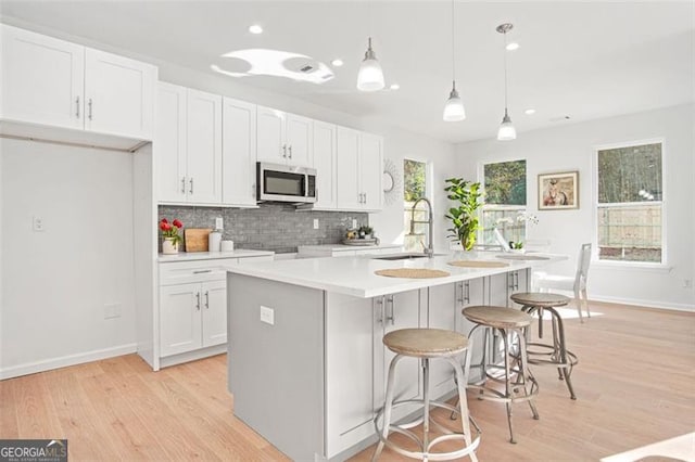 kitchen with sink, white cabinetry, tasteful backsplash, a center island with sink, and pendant lighting