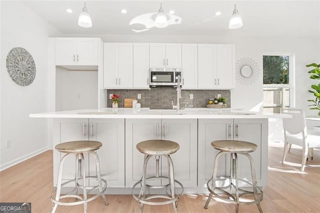 kitchen with a breakfast bar area, white cabinetry, hanging light fixtures, a center island with sink, and backsplash