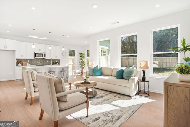 living room featuring a healthy amount of sunlight, sink, and light wood-type flooring