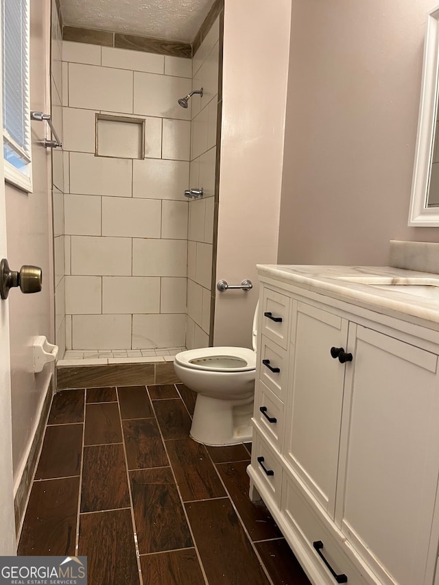 bathroom with tiled shower, vanity, a textured ceiling, and toilet