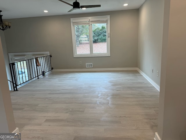 empty room with ceiling fan with notable chandelier and light wood-type flooring