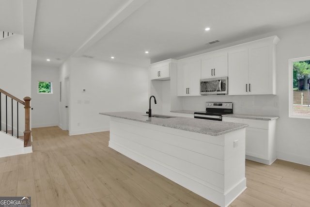 kitchen featuring a center island with sink, sink, light wood-type flooring, appliances with stainless steel finishes, and white cabinetry