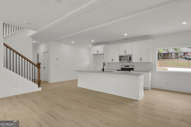 kitchen with white cabinets, stainless steel appliances, light hardwood / wood-style flooring, and an island with sink