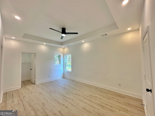 unfurnished room with a tray ceiling, ceiling fan, and light wood-type flooring