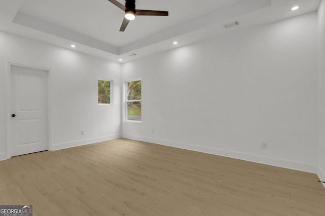 unfurnished room featuring ceiling fan, a tray ceiling, and light hardwood / wood-style flooring