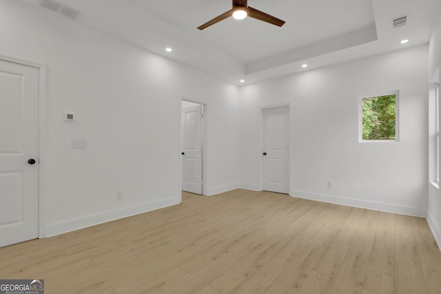 empty room featuring a tray ceiling, ceiling fan, and light wood-type flooring