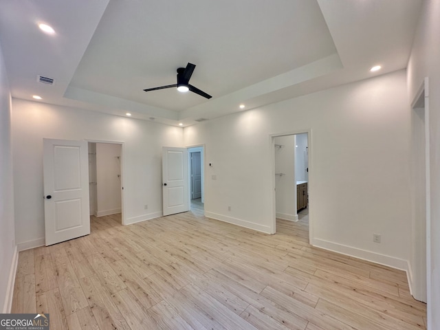 unfurnished bedroom featuring ceiling fan, a walk in closet, a raised ceiling, and light wood-type flooring