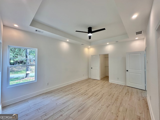 unfurnished bedroom with light hardwood / wood-style floors, a spacious closet, ceiling fan, and a tray ceiling