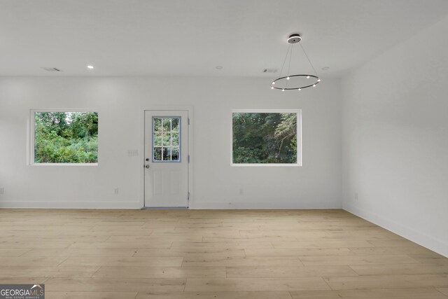 empty room with light hardwood / wood-style floors and an inviting chandelier