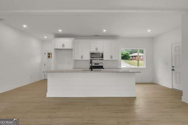 kitchen featuring white cabinetry, light stone countertops, a center island with sink, appliances with stainless steel finishes, and light wood-type flooring