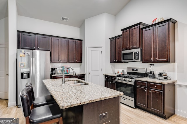 kitchen featuring light stone countertops, sink, stainless steel appliances, light hardwood / wood-style floors, and a kitchen island with sink