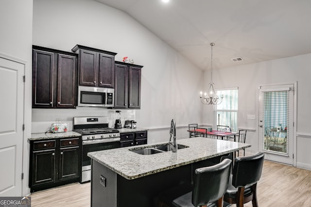 kitchen featuring sink, stainless steel appliances, an island with sink, decorative light fixtures, and vaulted ceiling