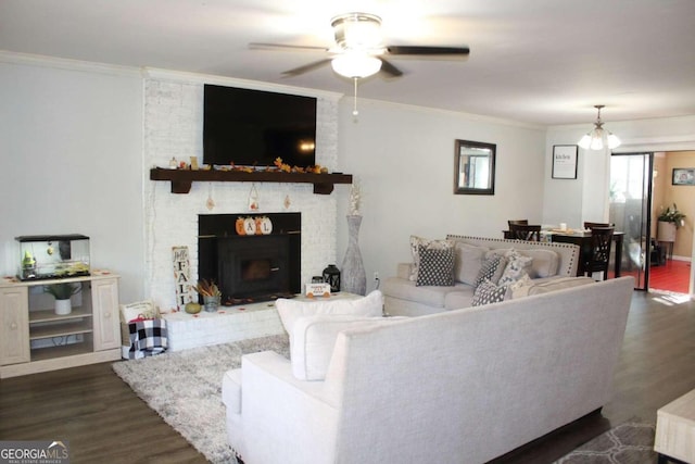 living room with ceiling fan with notable chandelier, dark hardwood / wood-style flooring, a brick fireplace, and crown molding