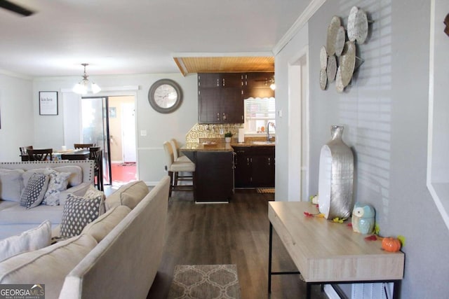 living room featuring sink, dark hardwood / wood-style flooring, ornamental molding, and a notable chandelier