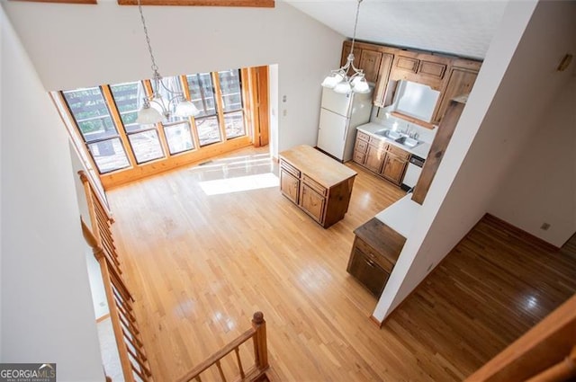 kitchen with sink, light hardwood / wood-style flooring, high vaulted ceiling, a chandelier, and decorative light fixtures