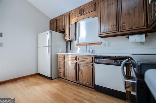 kitchen featuring white appliances, light hardwood / wood-style floors, vaulted ceiling, and sink