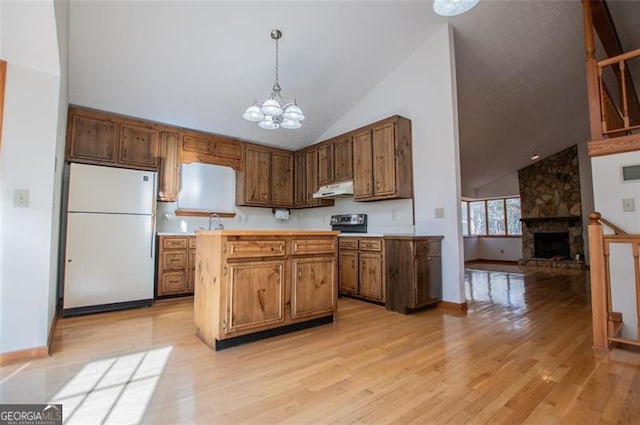 kitchen featuring light wood-type flooring, an inviting chandelier, white fridge, a stone fireplace, and hanging light fixtures