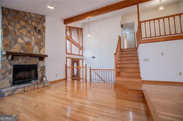 living room with hardwood / wood-style flooring, a stone fireplace, and beamed ceiling